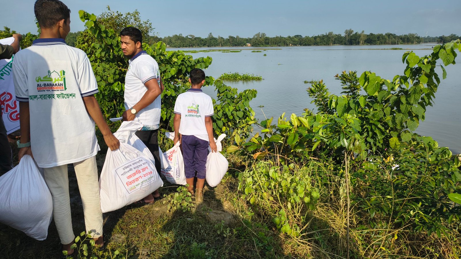 বন্যার পানির পাশ দিয়ে ত্রাণের বস্তা বয়ে নিচ্ছেন স্বেচ্ছাসেবকরা
